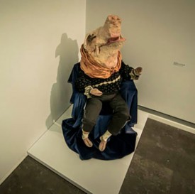 Installation shot of the exhibition under review, showing a papier maché pig in satin clothes.